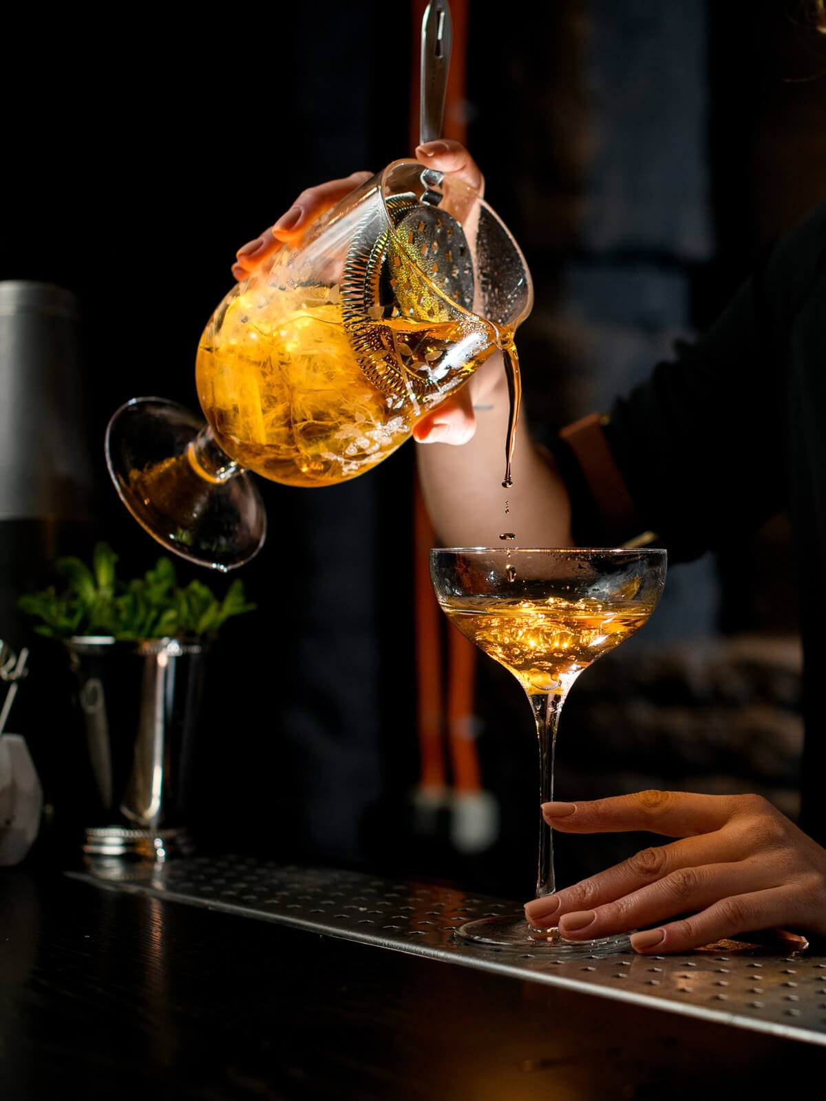 An unseen bartender pours a golden colored cocktail.