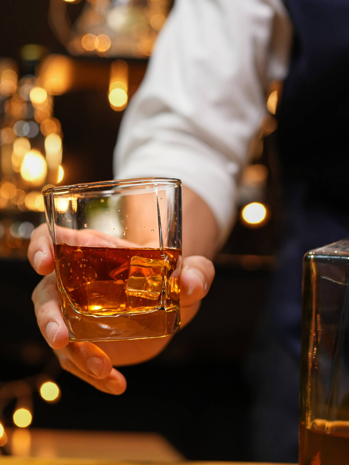 A bartender presenting a half-full whiskey glass.